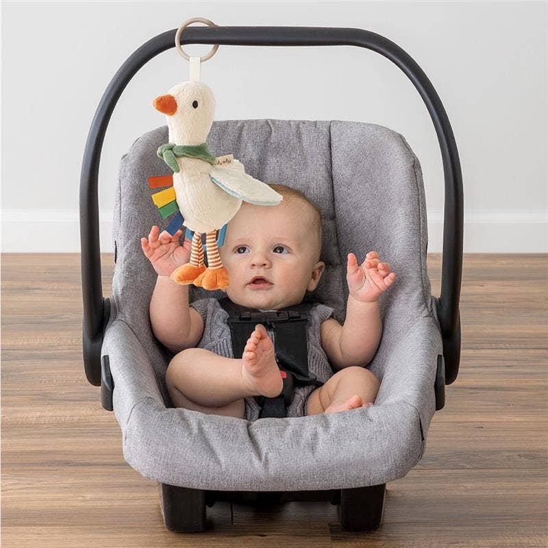 Baby in a car seat with a colorful goose toy hanging above
