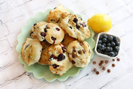 Blueberry scones on a green plate with a lemon and blueberries on a white wooden surface