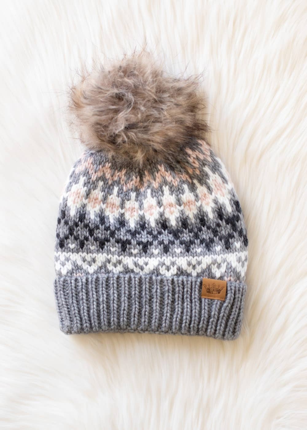 Knitted beanie with a fur pom-pom on a white textured background