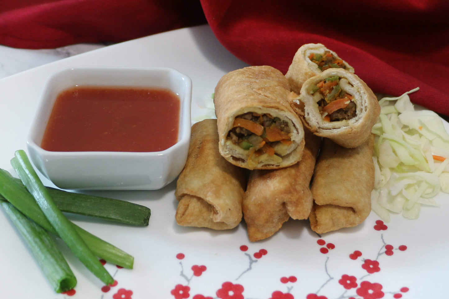 Spring rolls with a side of dipping sauce and vegetables on a decorative plate.
