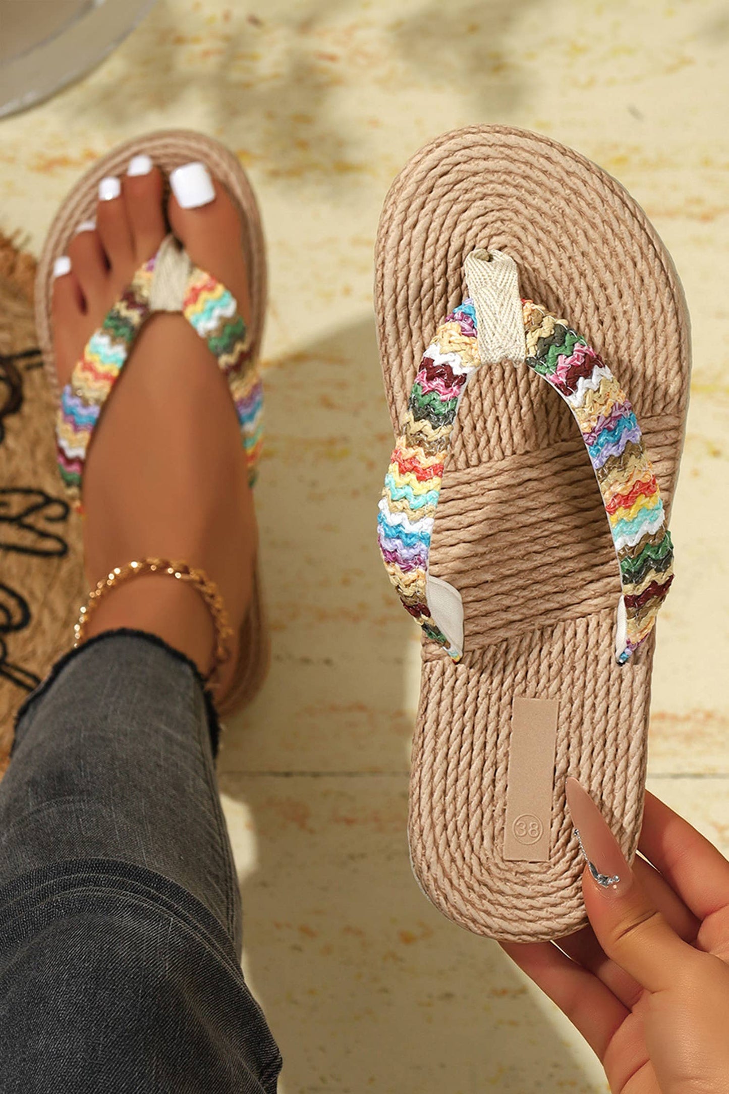 Beige sandals with colorful straps held by a hand on a textured surface