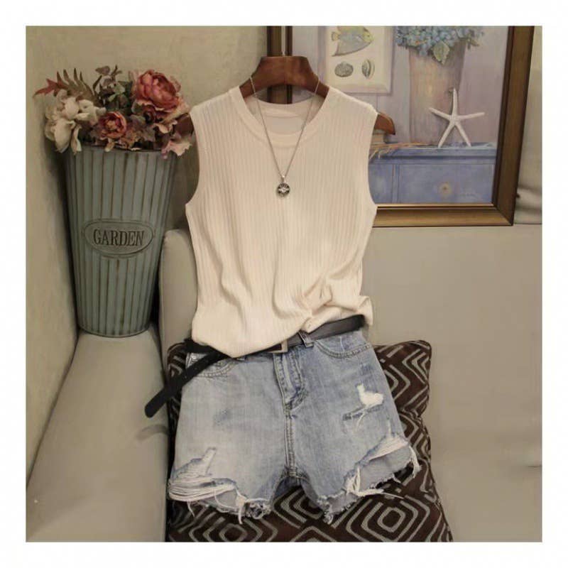White sleeveless top and denim shorts on a hanger with decorative elements in the background.
