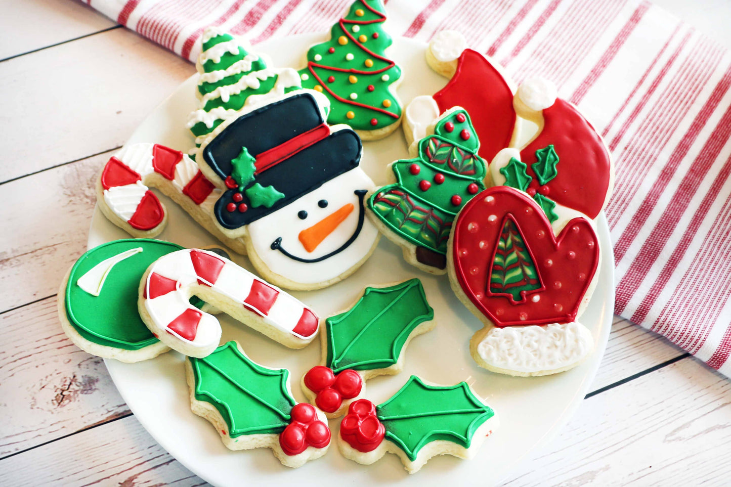 Decorative Christmas cookies on a plate with a red and white striped towel in the background.