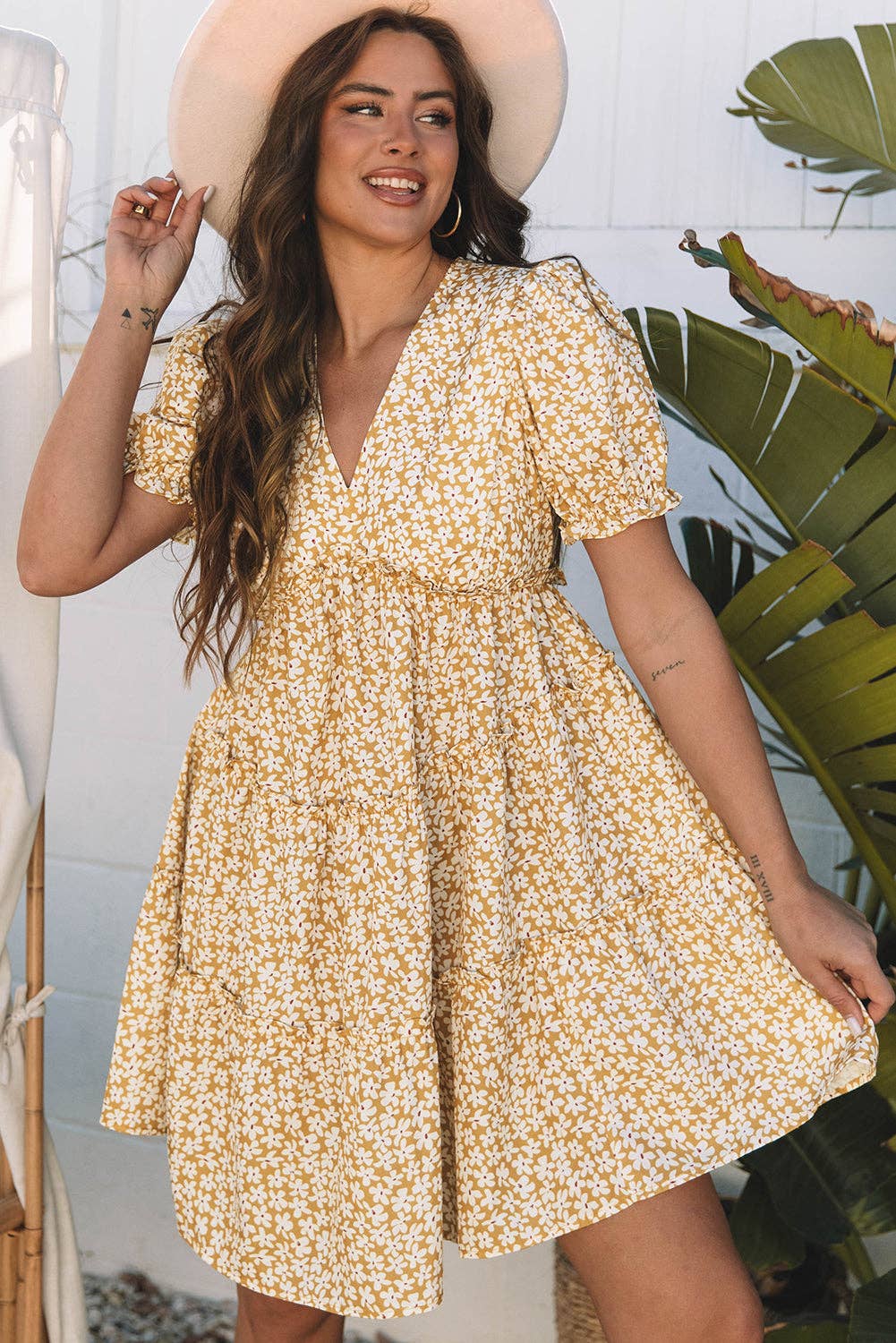 Woman wearing a yellow floral dress with a plant in the background