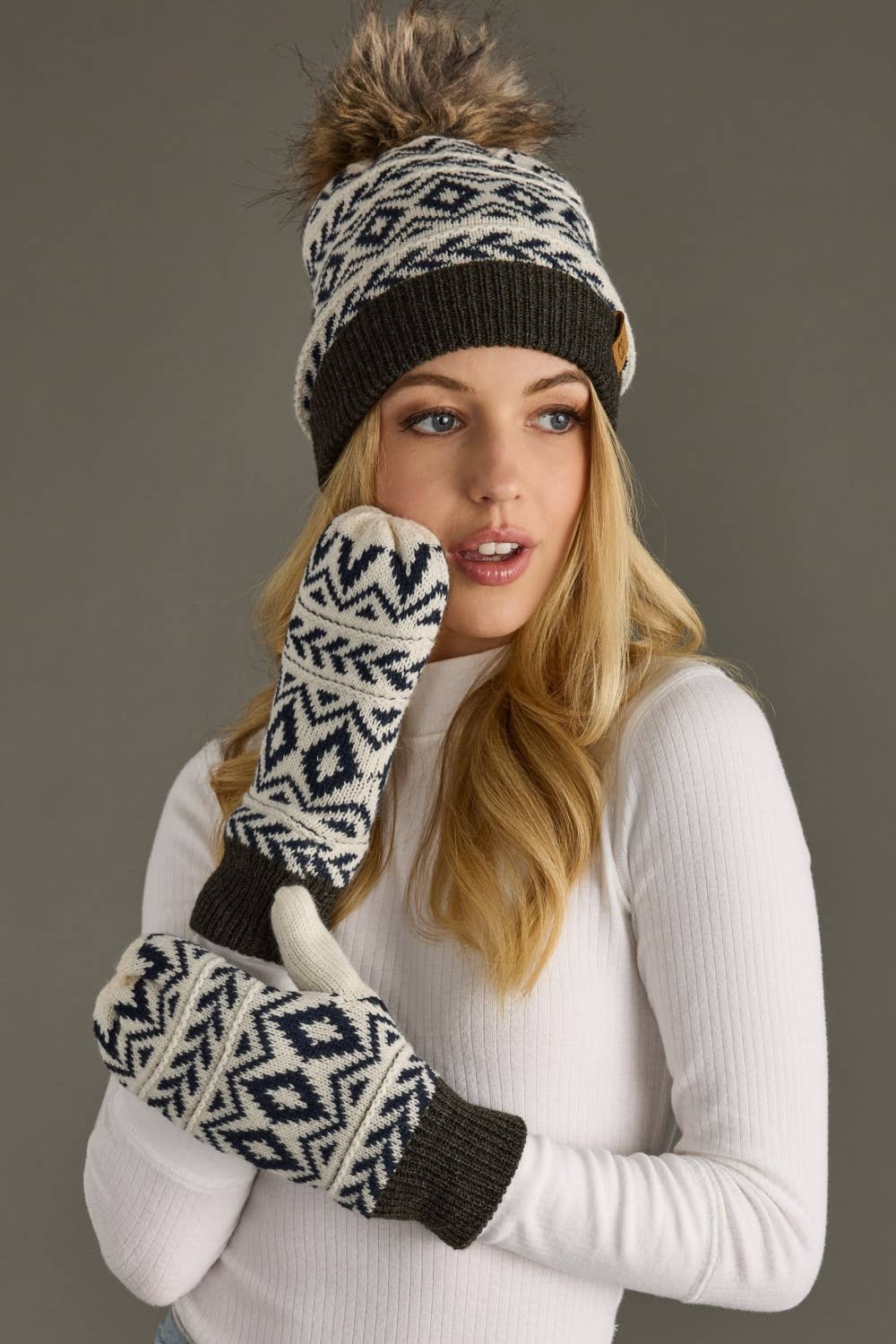Woman wearing a patterned beanie and mittens against a neutral background