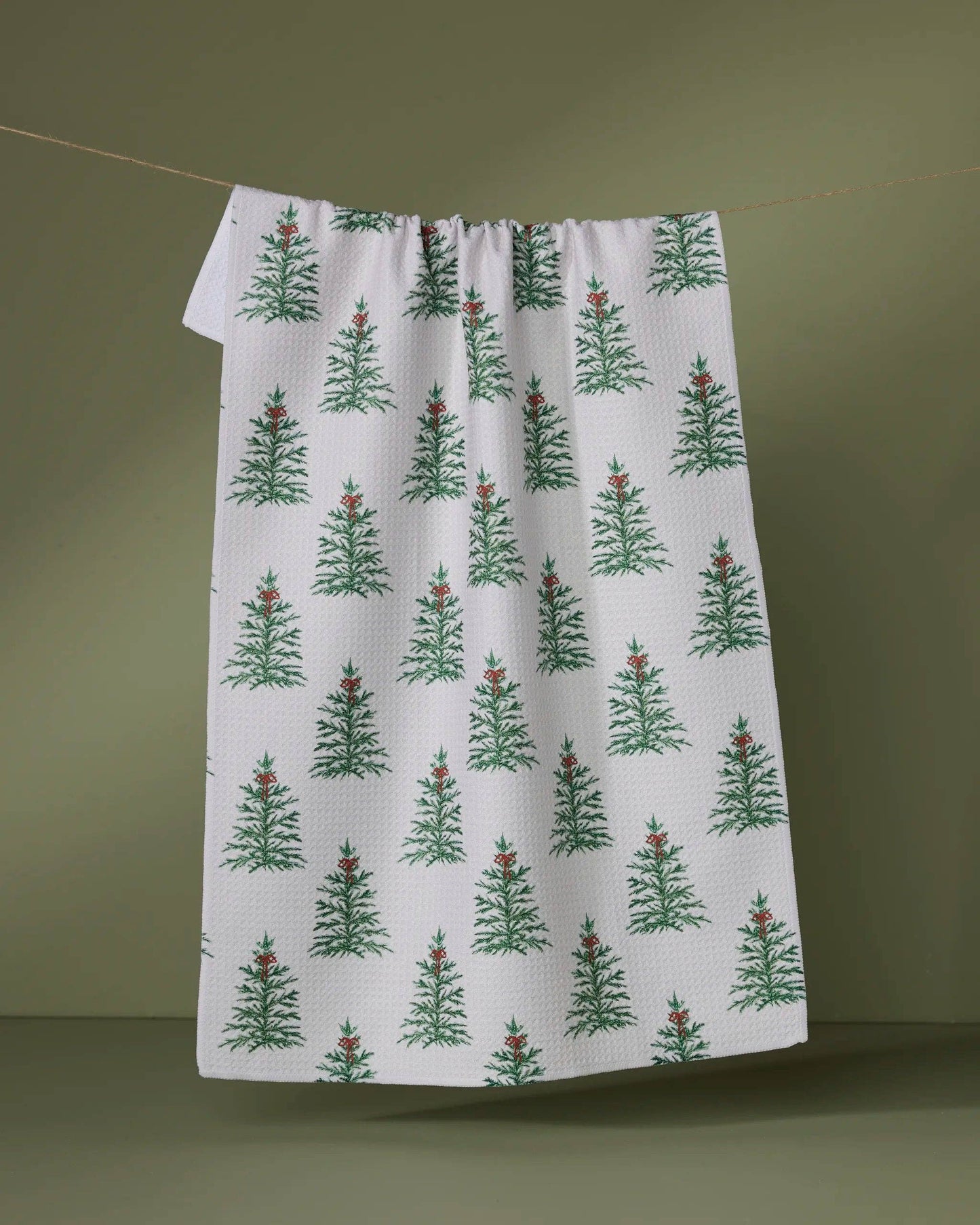 Geometry Tea Towel l with green tree pattern hanging on a line against a green background