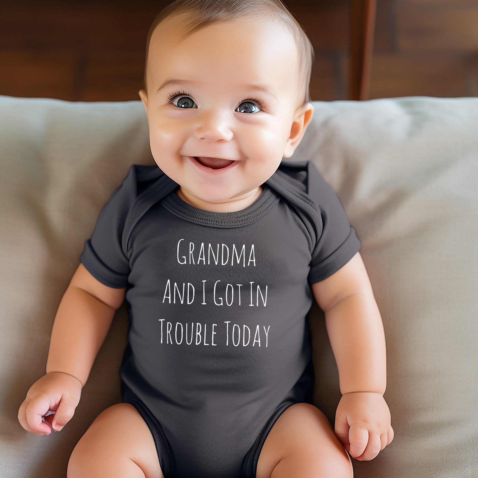 Baby wearing a dark gray onesie with text, sitting on a beige couch.