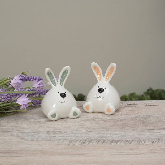 Two ceramic rabbit figures on a wooden surface with flowers in the background