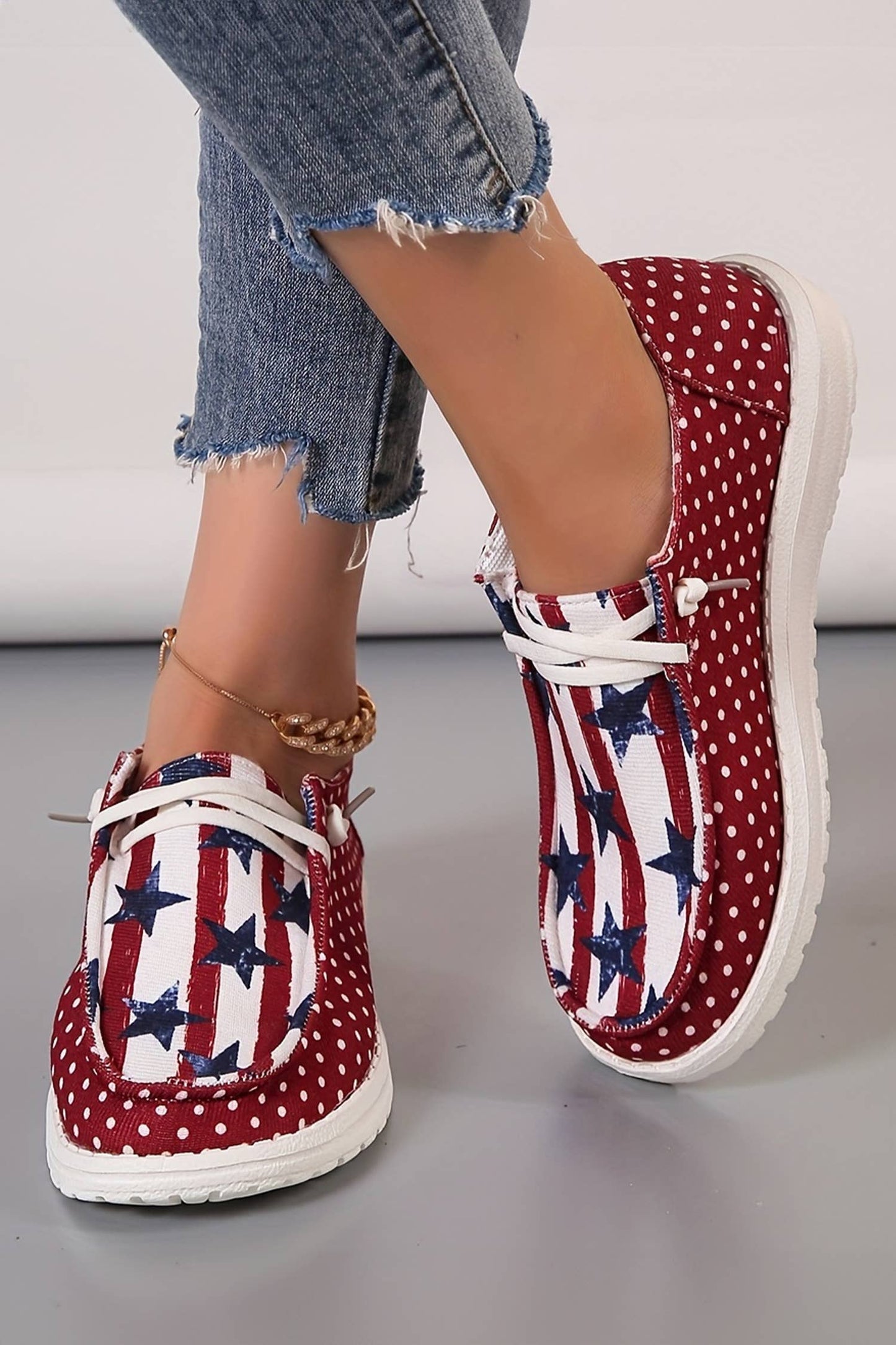 Red polka dot shoes with American flag pattern worn with denim jeans on a neutral background