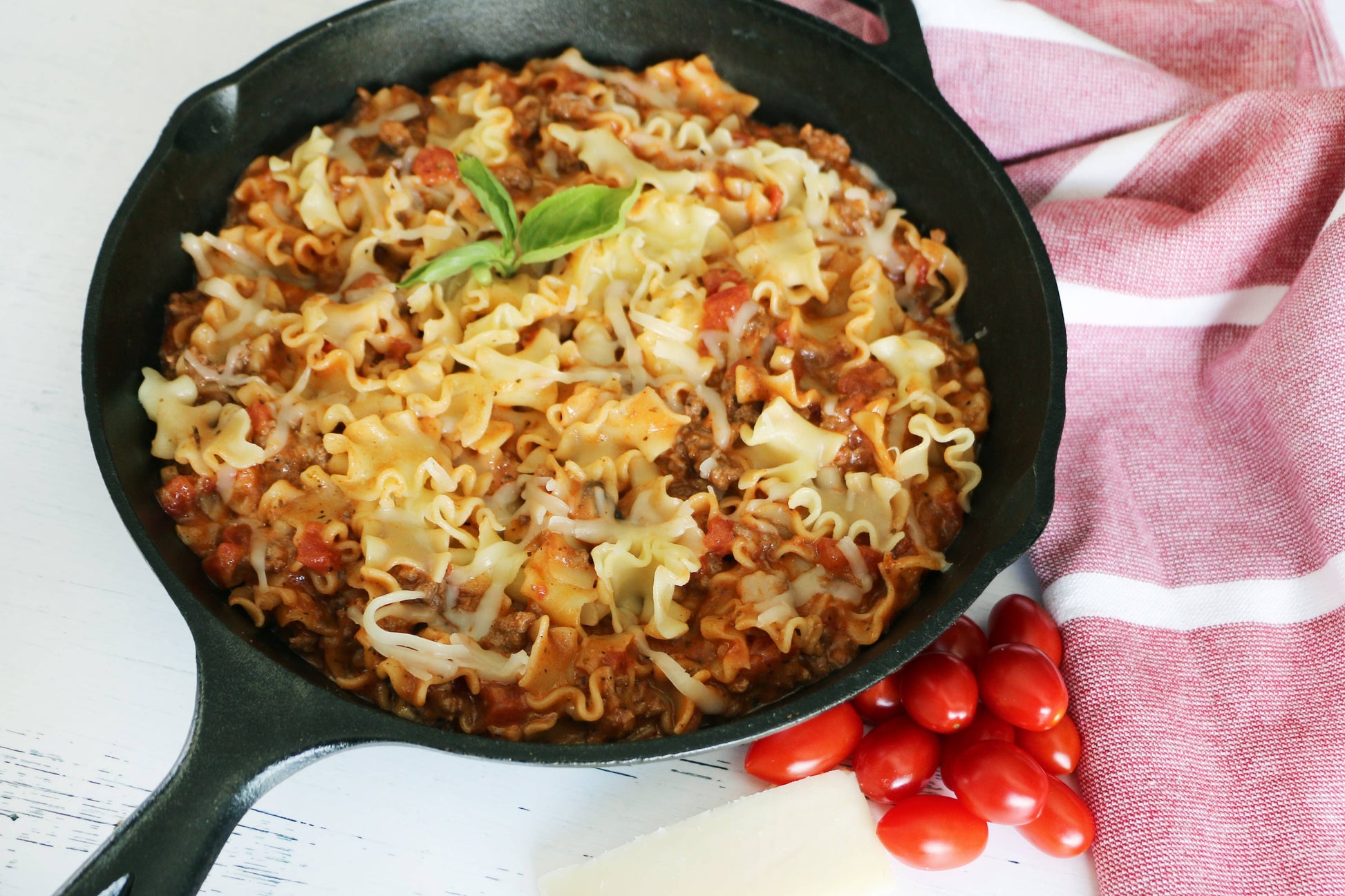 Pasta dish in a black skillet on a white surface with a red cloth