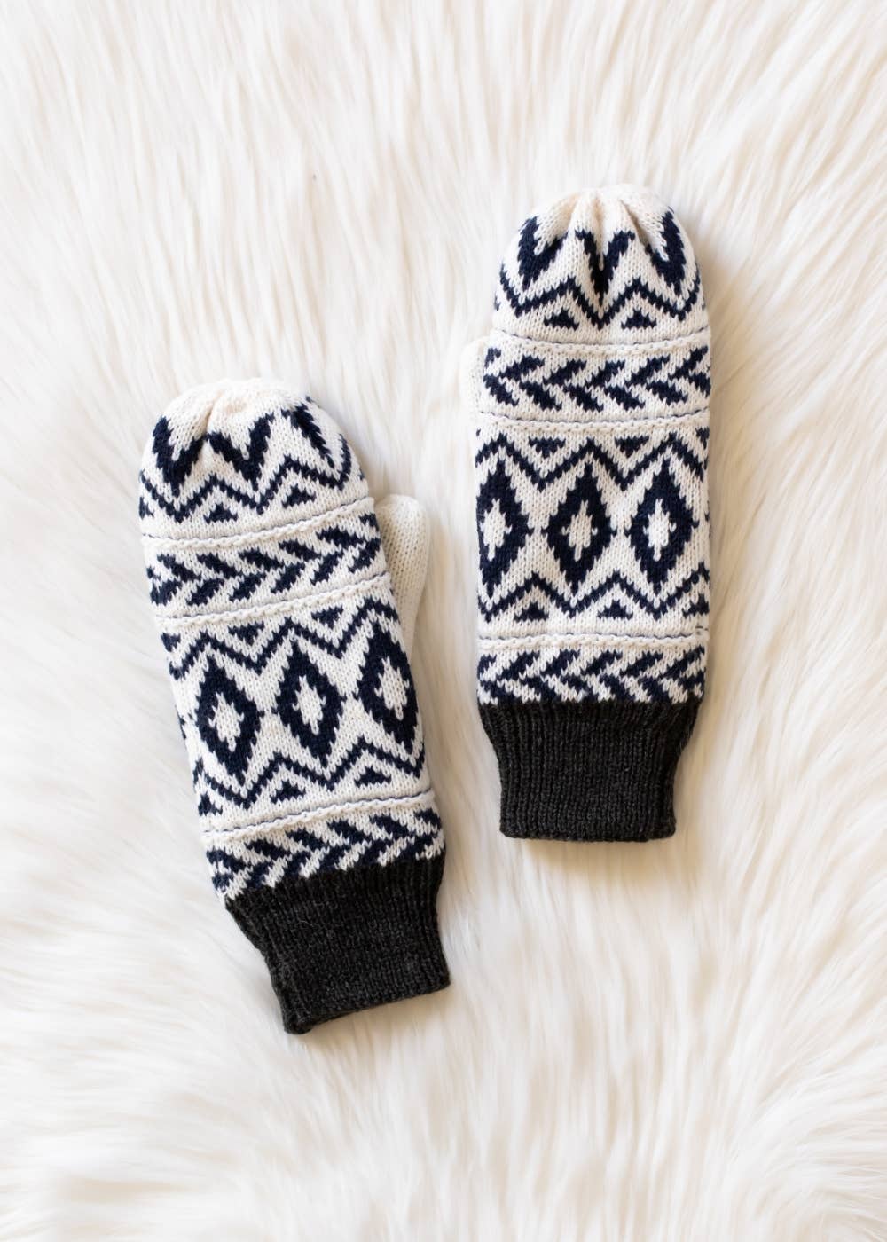 Pair of navy and white patterned mittens with gray cuff on a white textured surface