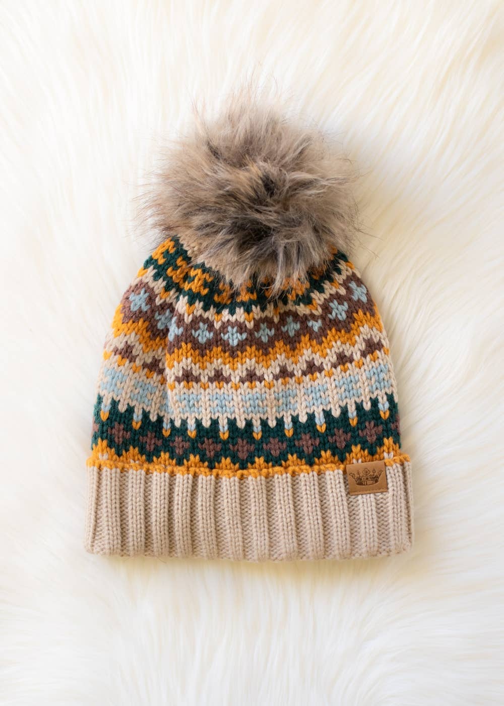 Knitted beanie with a pattern and fur pom-pom on a white background