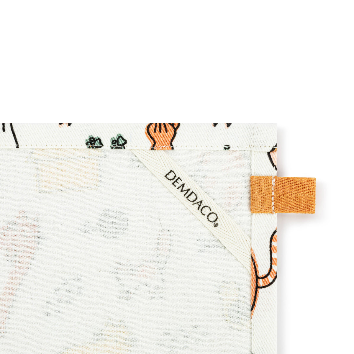 Close-up of a Demdaco cotton towel corner showing a white fabric base with a light gray animal print, an orange tab, and the Demdaco brand label.