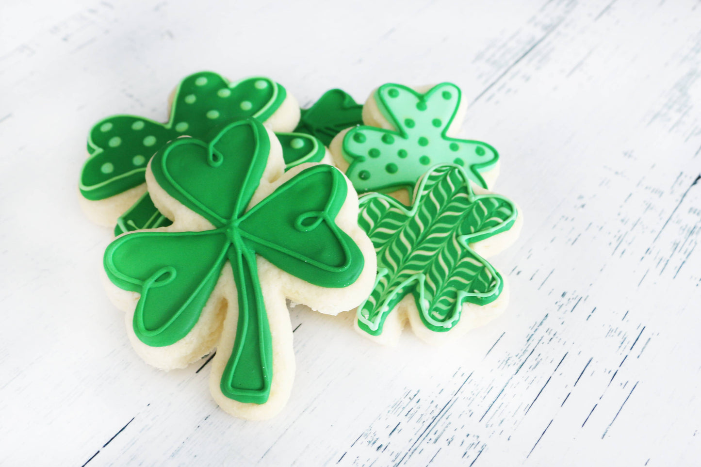 Decorative cookies shaped like shamrocks on a white wooden surface