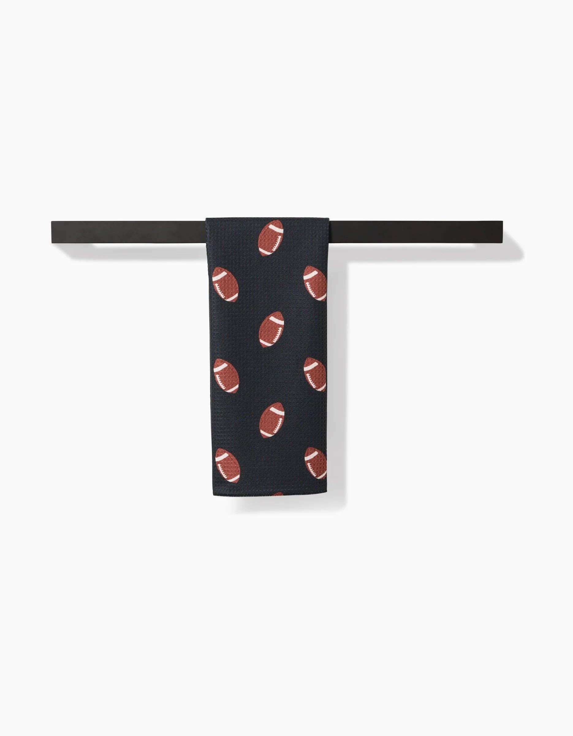 Black Geometry brand kitchen tea towel with brown football pattern on a white background hanging on a black towel bar