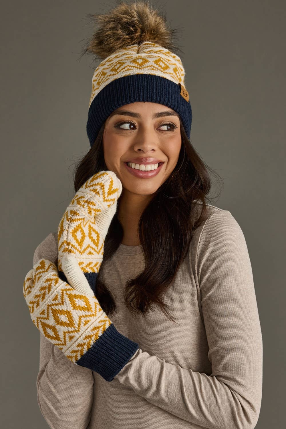 Woman wearing a patterned beanie, scarf, and mittens against a gray background
