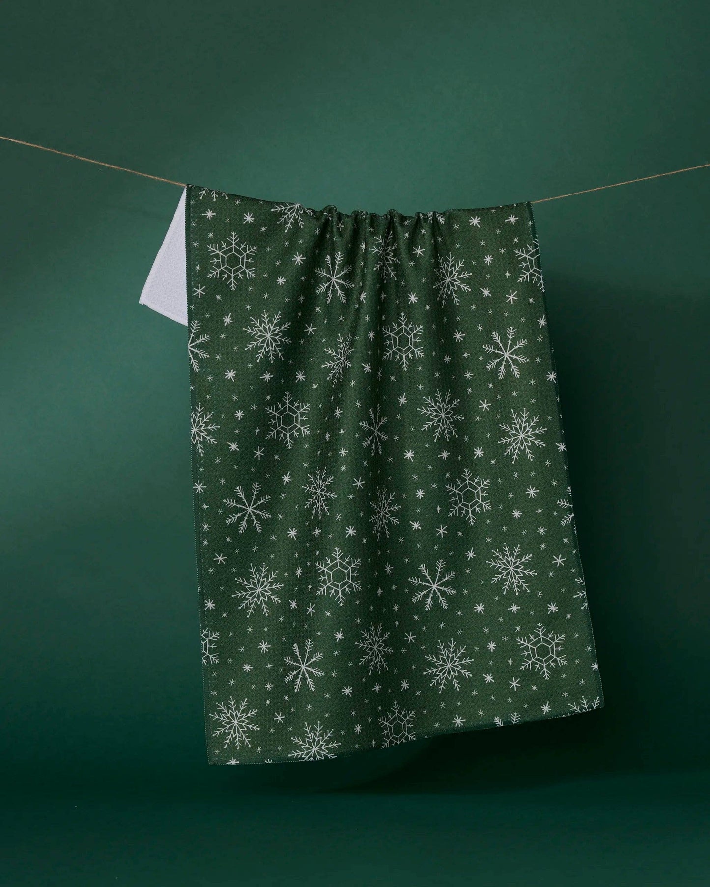 Geometry Tea Towel Green fabric with snowflake pattern hanging on a line against a green background