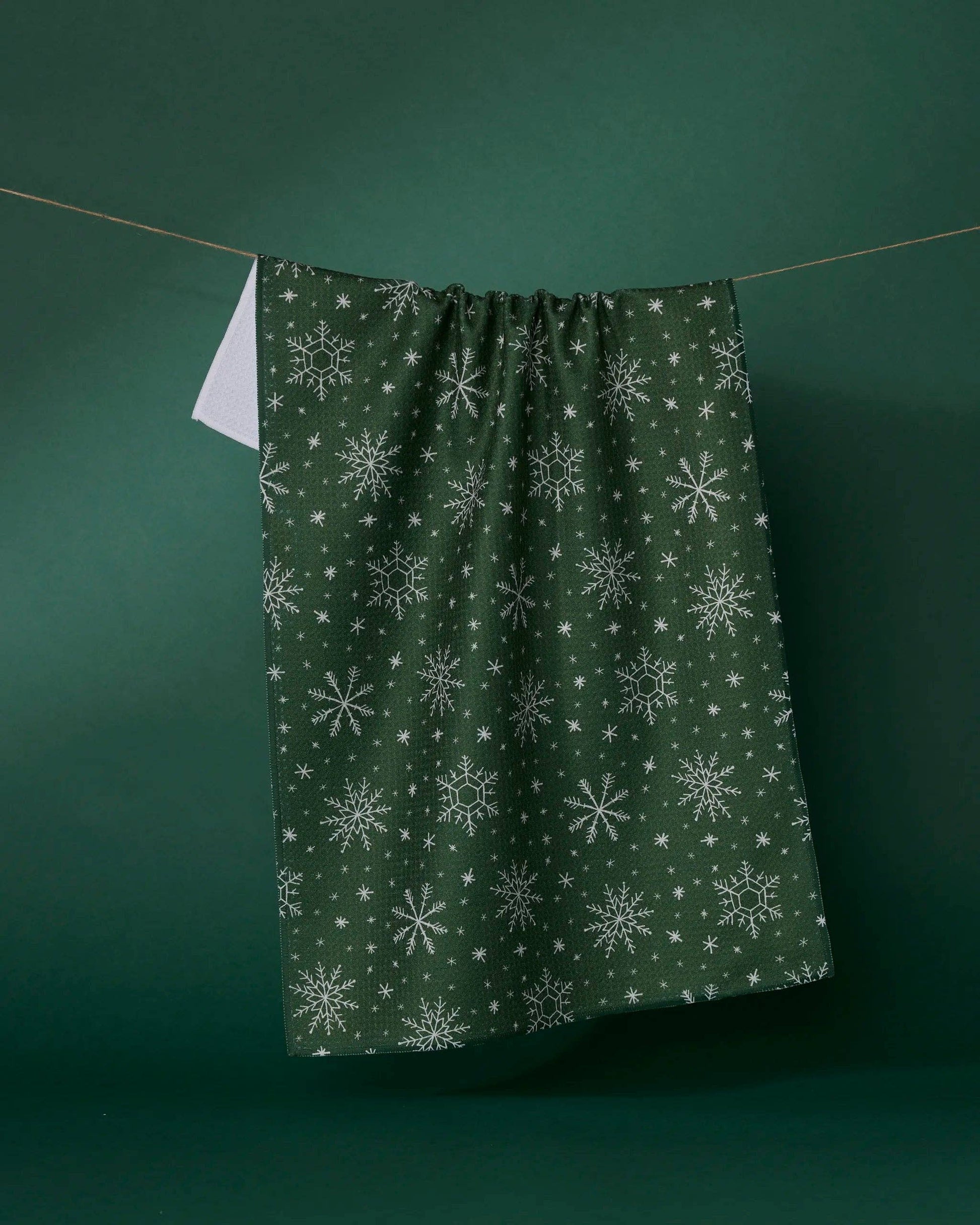 Geometry Tea Towel Green fabric with snowflake pattern hanging on a line against a green background