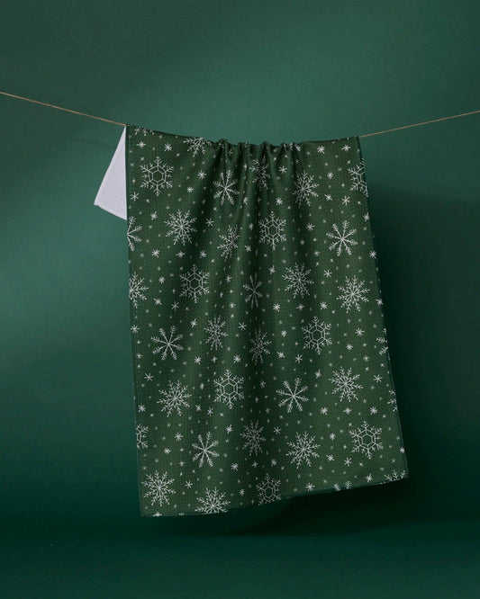 Geometry Tea Towel Green fabric with snowflake pattern hanging on a line against a green background