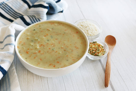 White bowl of soup on a wooden table with a wooden spoon and small containers of ingredients.