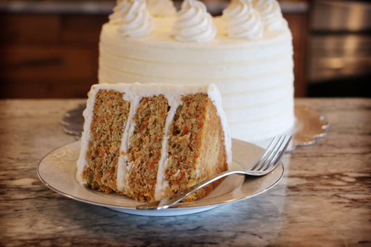 Carrot cake with white frosting on a plate with a fork, set against a kitchen background.