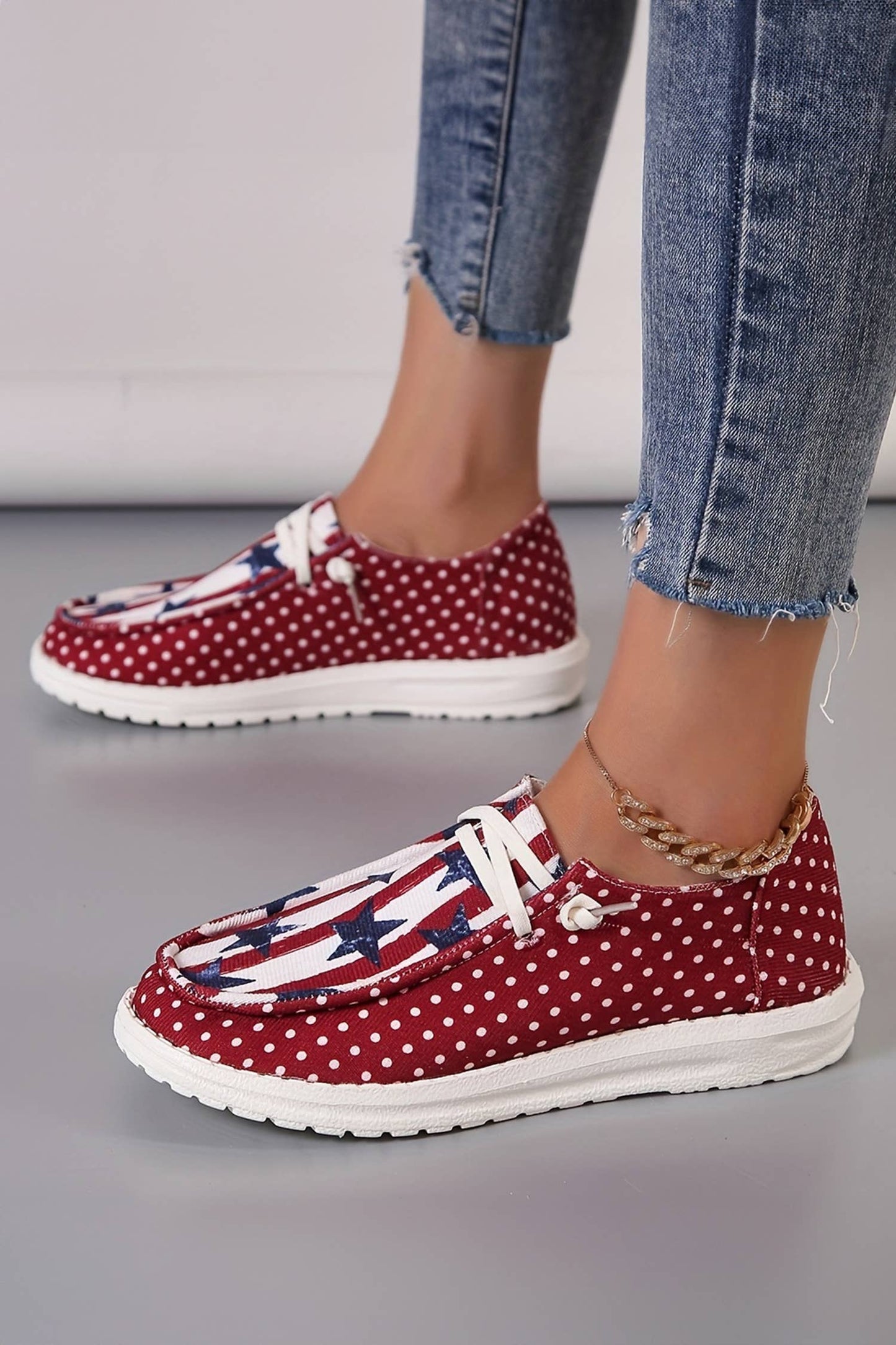 Red polka dot shoes with American flag design worn with blue jeans on a gray floor.