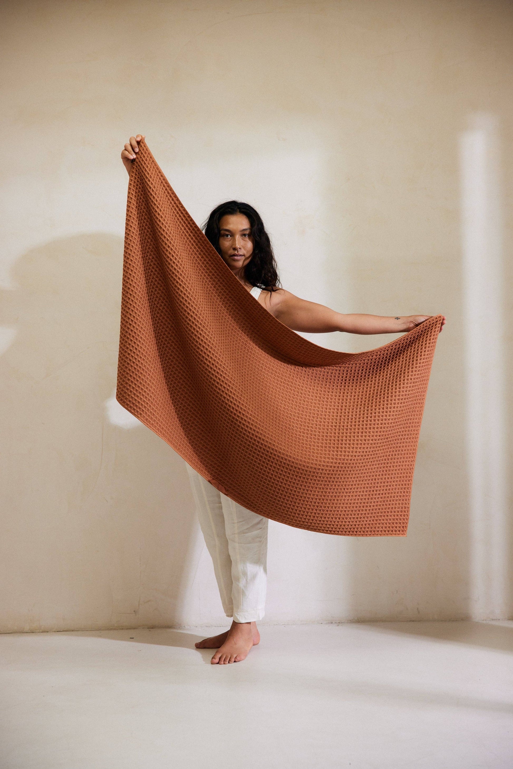 Woman holding a large brown textured blanket against a plain background Geometry Waffle Bath Towel Clay 