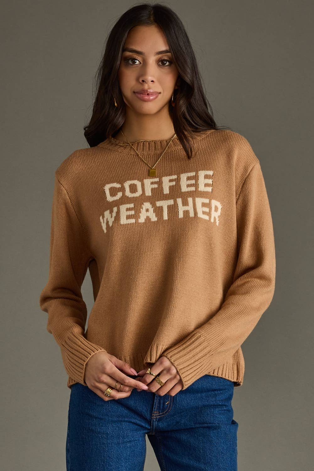 Woman wearing a brown sweater with 'COFFEE WEATHER' text against a gray background