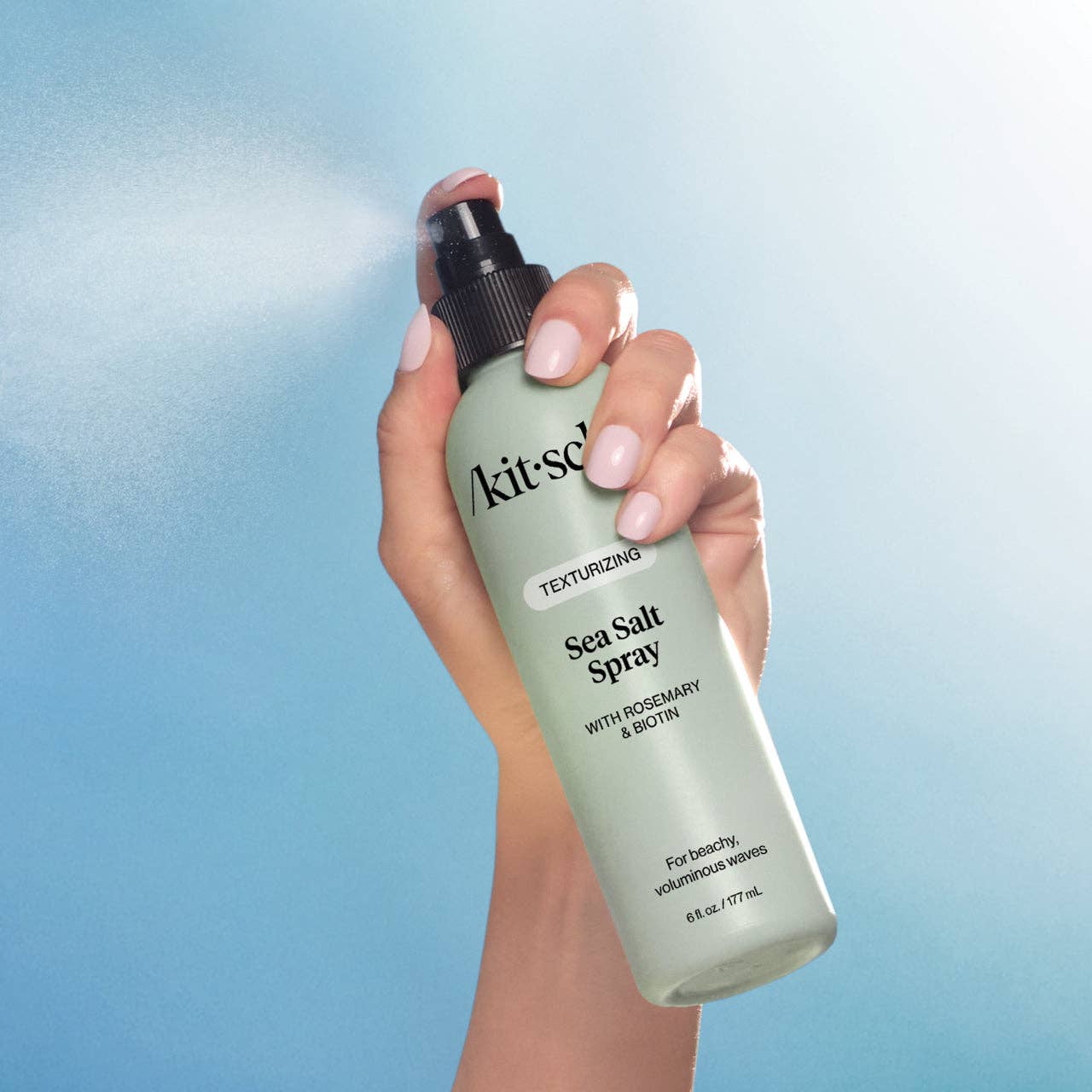 Hand holding a bottle of Kit-sch Sea Salt Spray against a blue gradient background