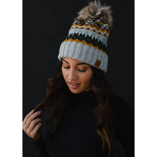 Woman wearing a patterned knit beanie with a pom-pom on a black background
