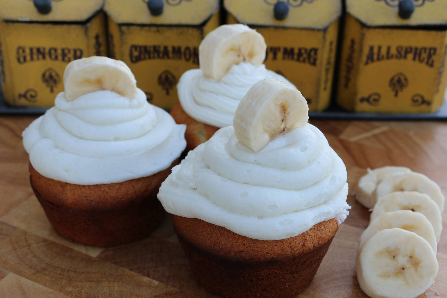 Banana cupcakes with white frosting on a wooden surface with banana slices.
