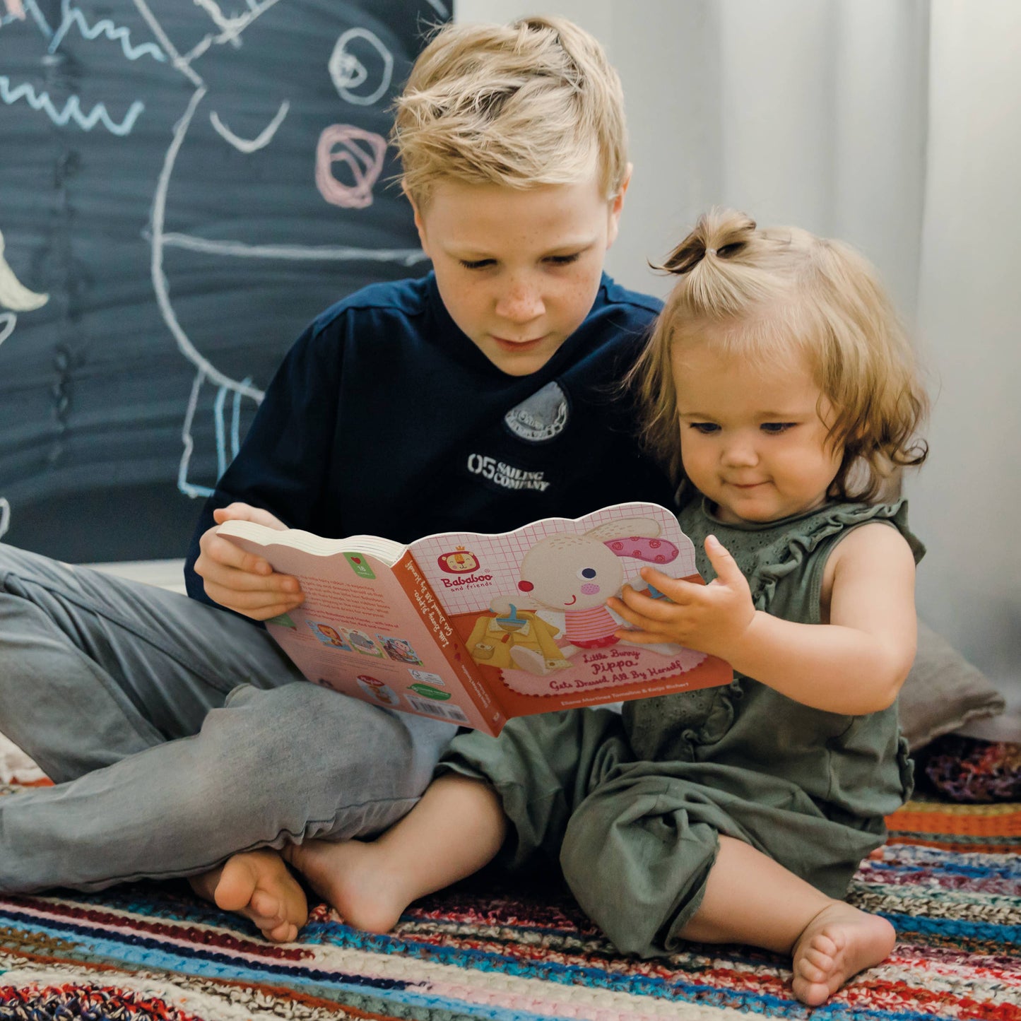 Two children sitting on a colorful rug reading a book together.