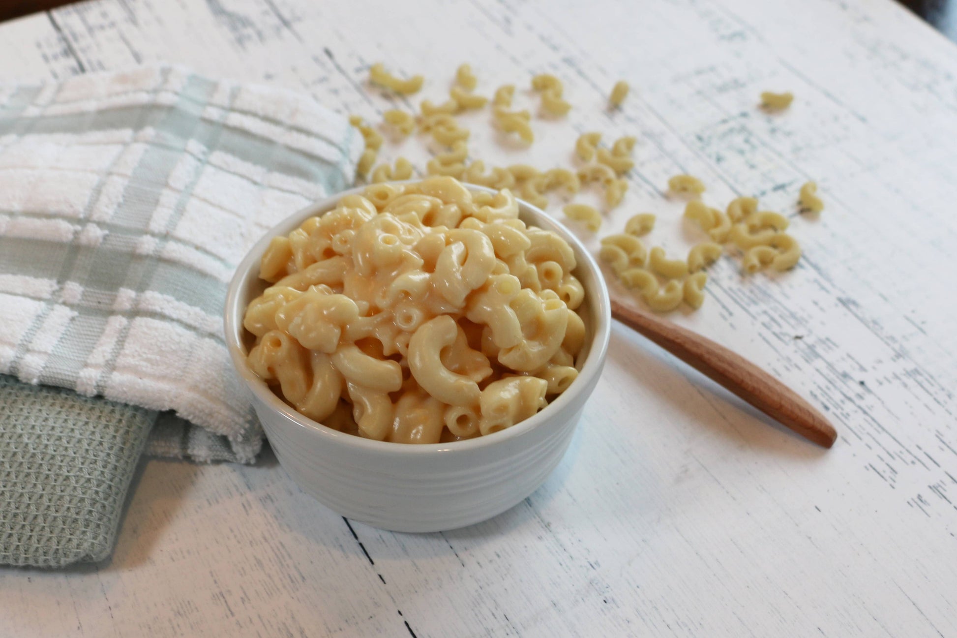 White bowl filled with macaroni and cheese on a wooden surface with a checkered cloth.