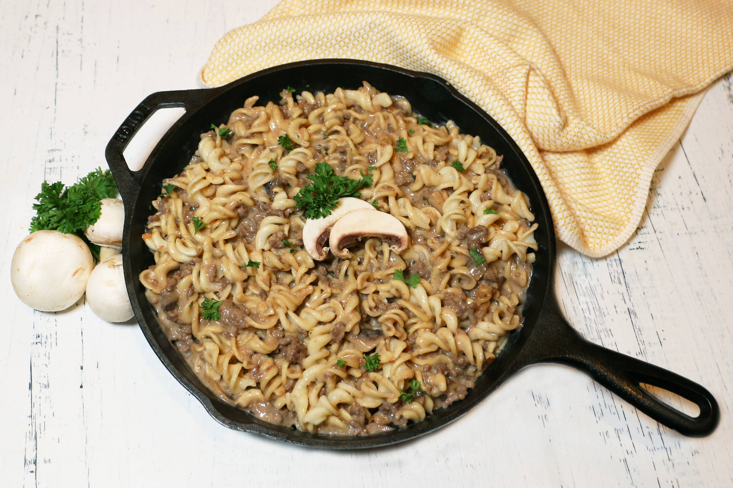 Pasta dish with mushrooms in a black skillet on a wooden surface