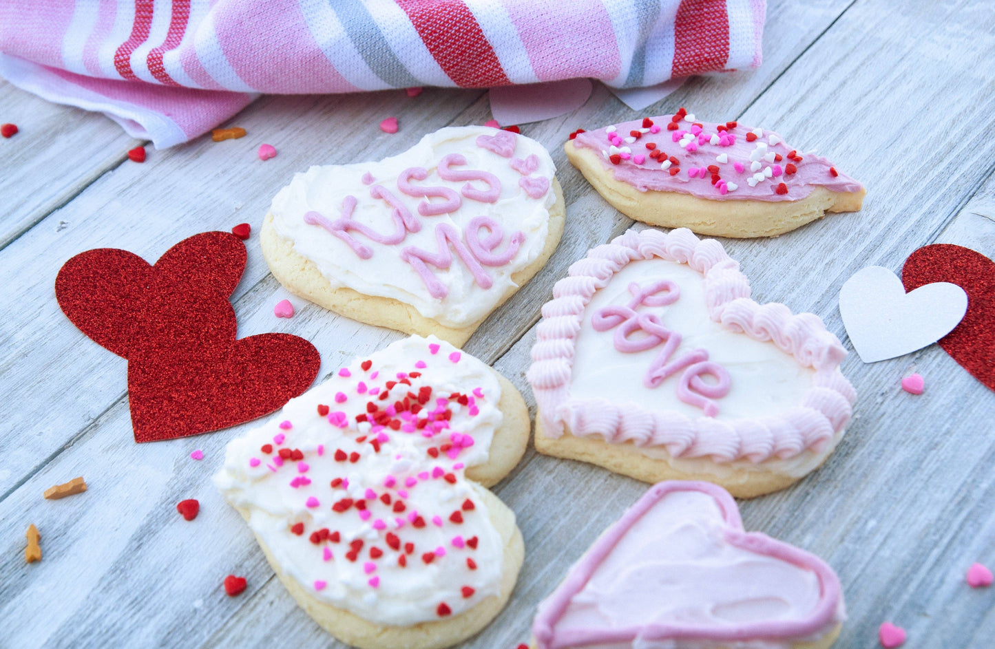 Heart-shaped cookies with pink and white icing on a wooden surface with heart decorations.