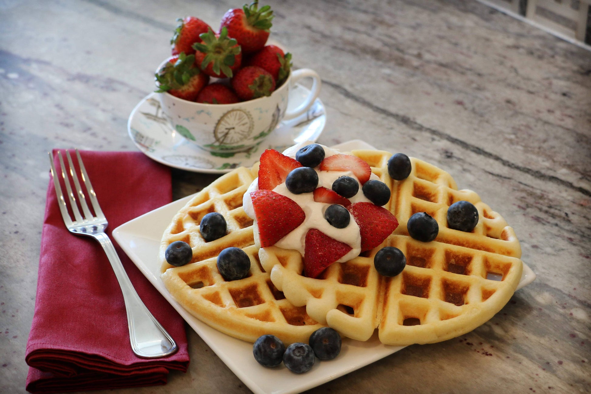 Heart-shaped waffles with berries on a wooden table with a cup of strawberries.