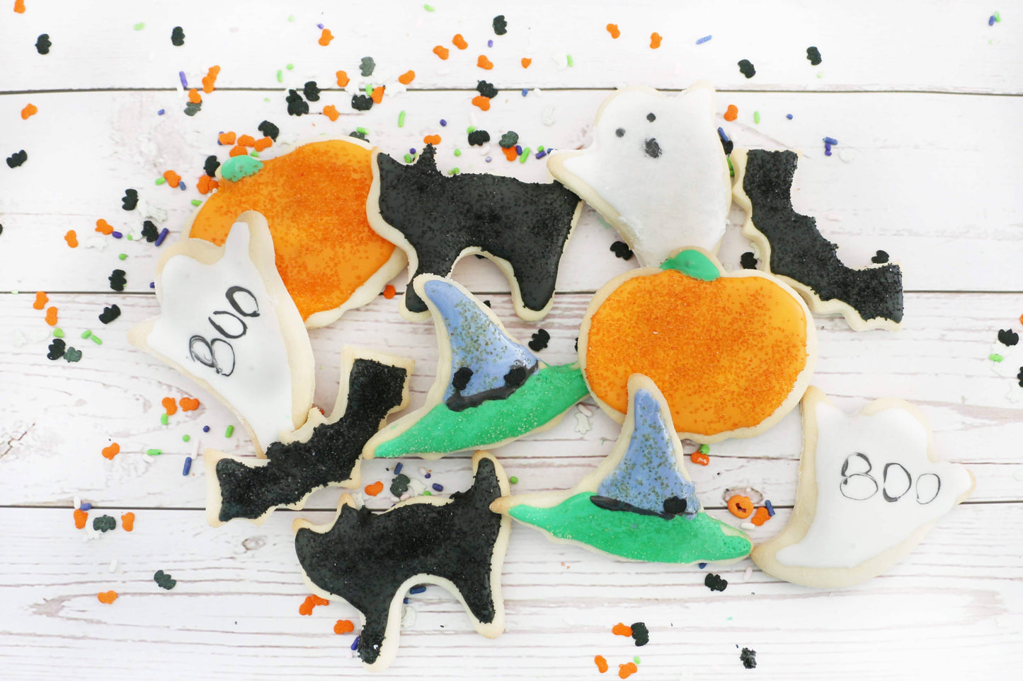 Halloween-themed cookies with pumpkins, bats, and witches' hats on a wooden surface.
