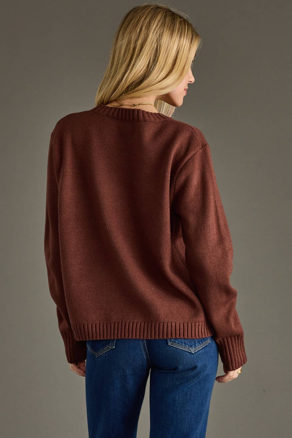 Person wearing a brown sweater and blue jeans against a gray background
