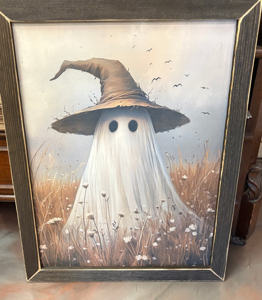 Framed artwork of a ghost wearing a witch's hat in a field with a wooden frame.