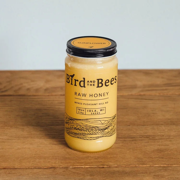 Jar of Bird and the Bees raw honey on a wooden surface with a light background