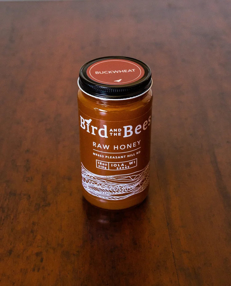 Jar of Bird and the Bean raw honey on a wooden surface. Buckwheat