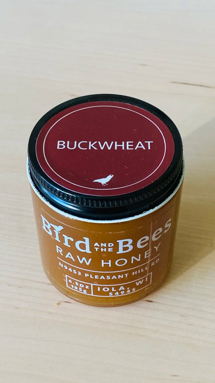 Jar of 'Buckwheat' raw honey by 'Bee & The Wild' on a wooden surface.