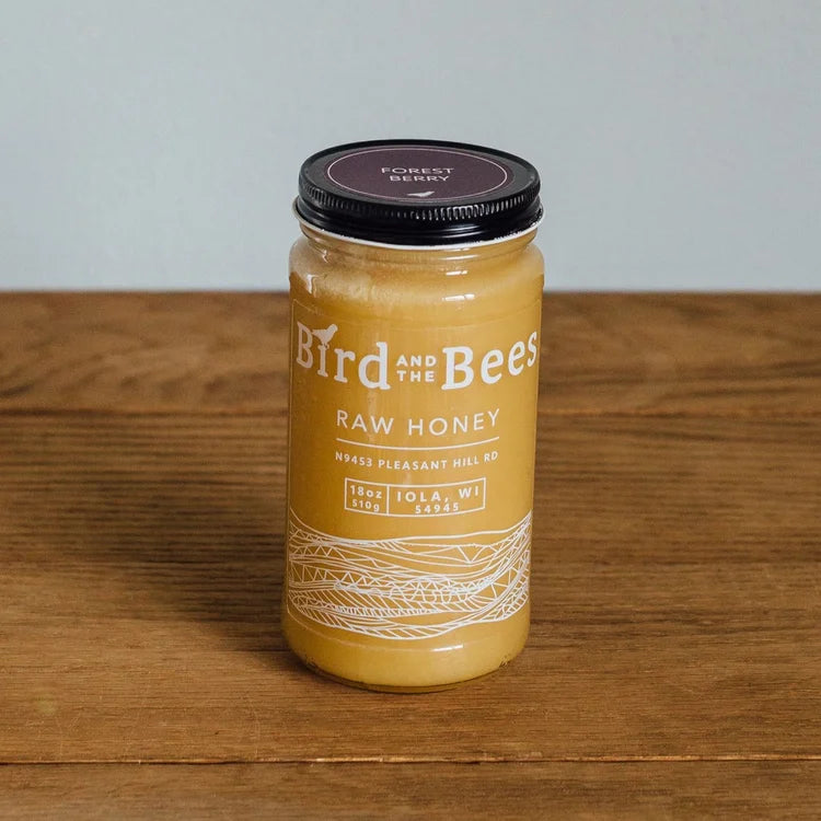 Jar of Bird and the Bees raw honey on a wooden surface with a gray background