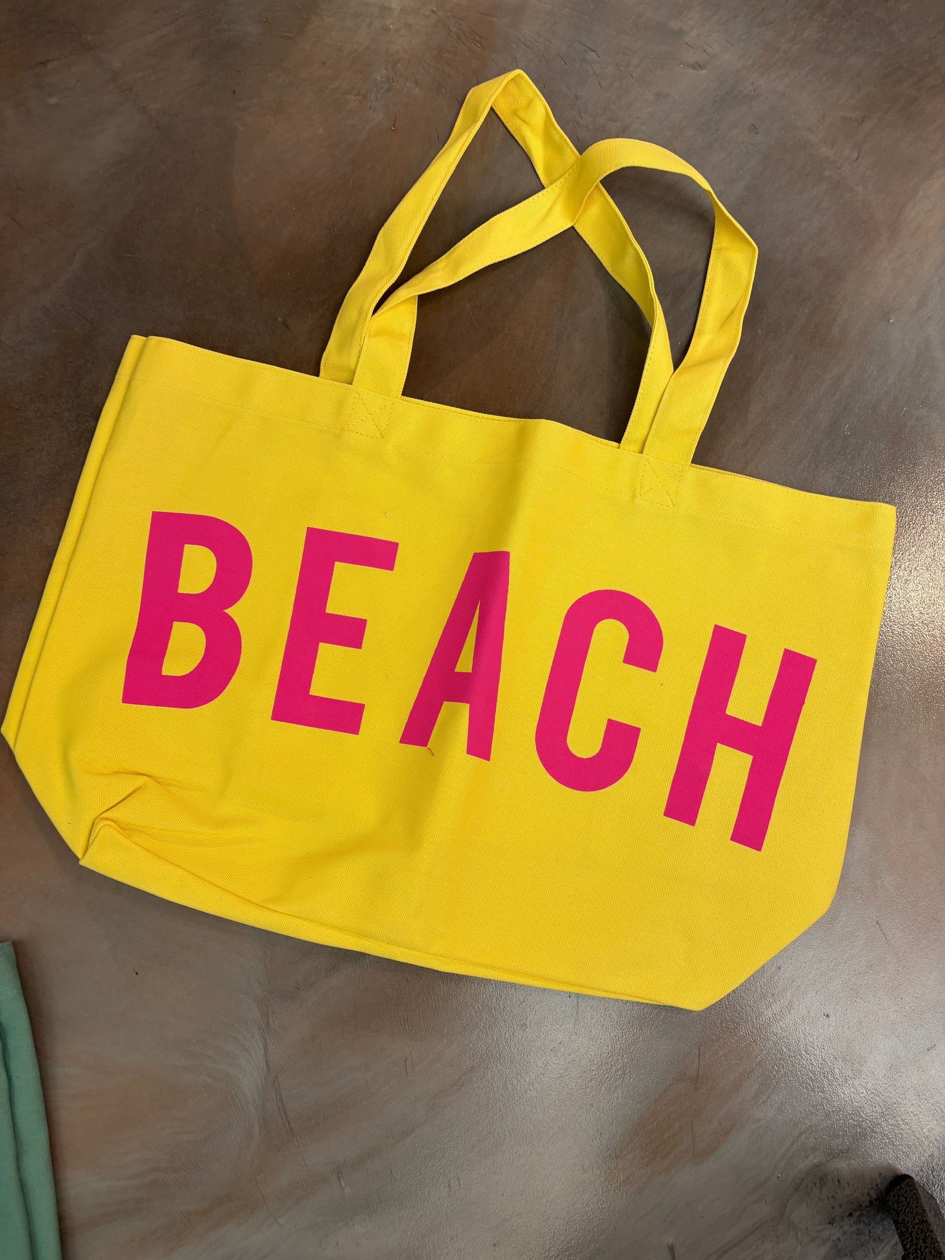 Yellow tote bag with 'BEACH' written in pink on a metallic surface