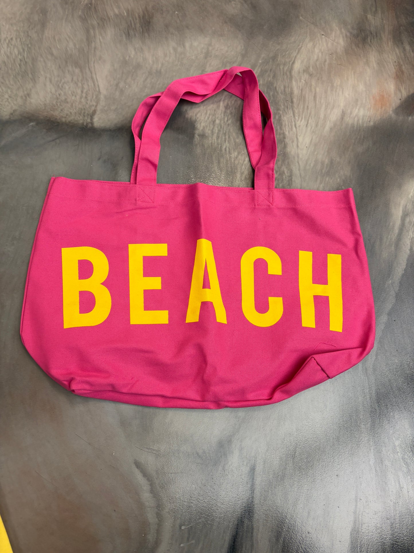 Pink tote bag with 'BEACH' in yellow on a gray surface