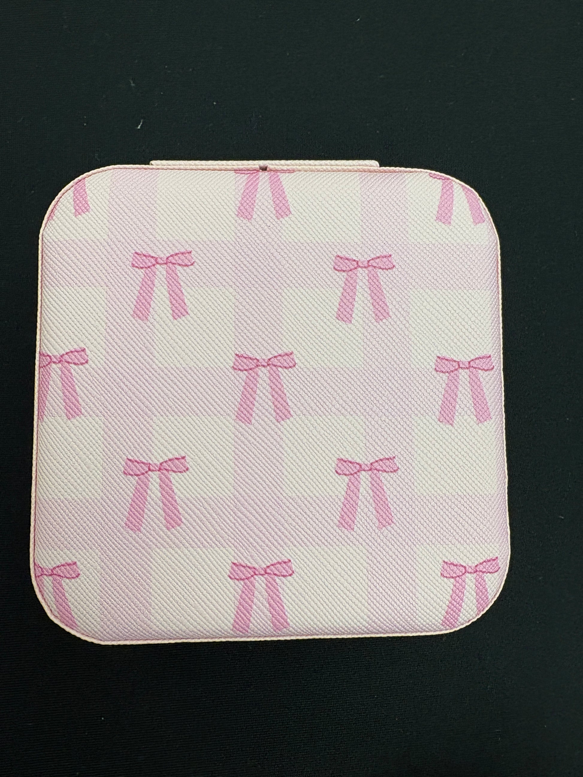 Square pink jewelry pouch with bow pattern on a black background