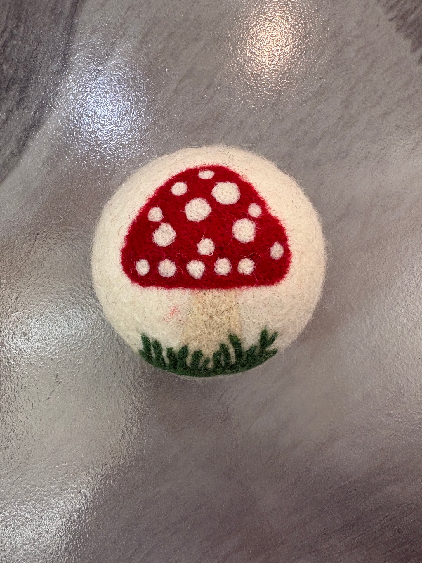 white wool dryer ball with red mushroom design on a metallic surface