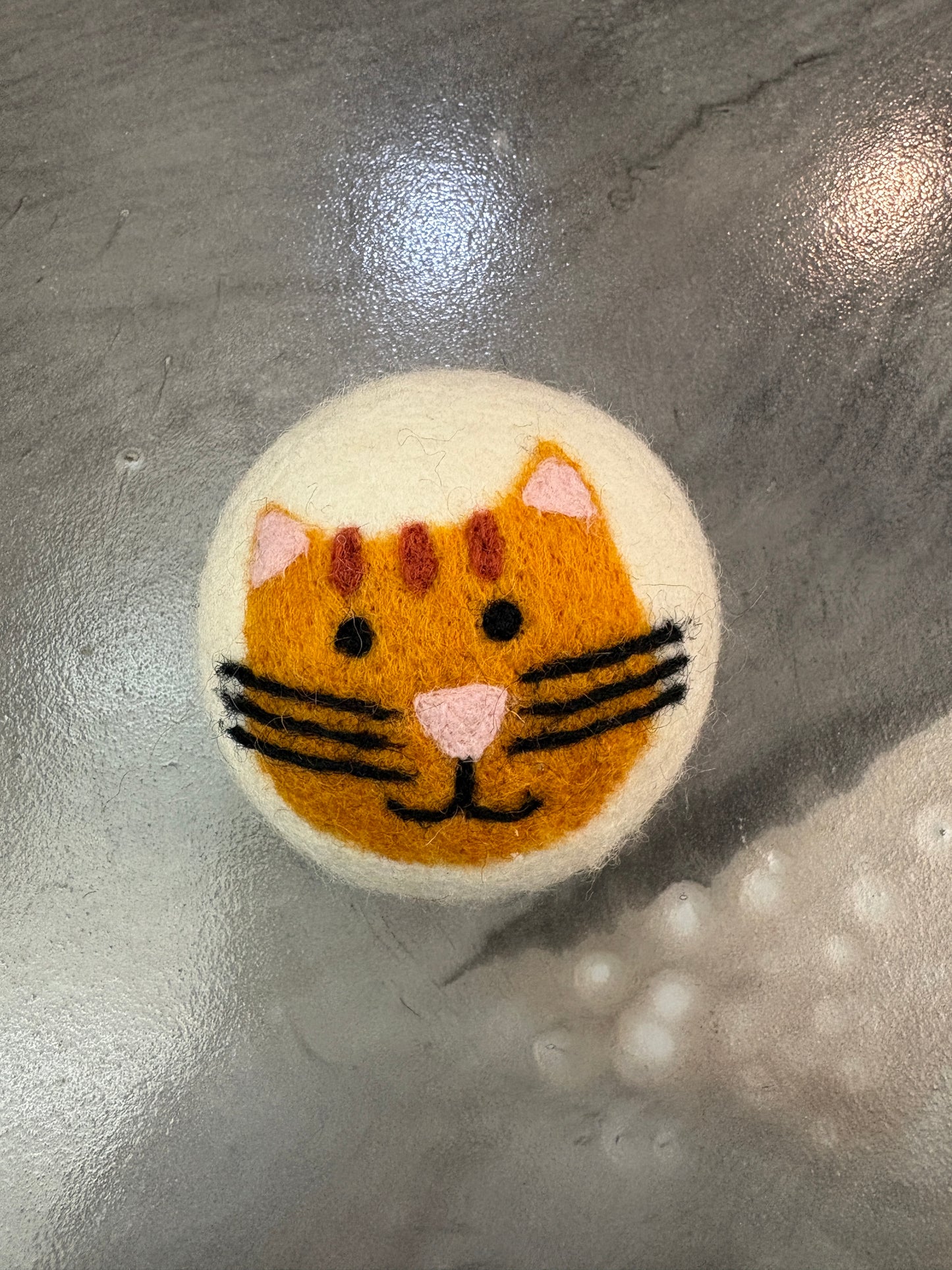 white wool felted dryer ball with a orange cat design on a metallic surface