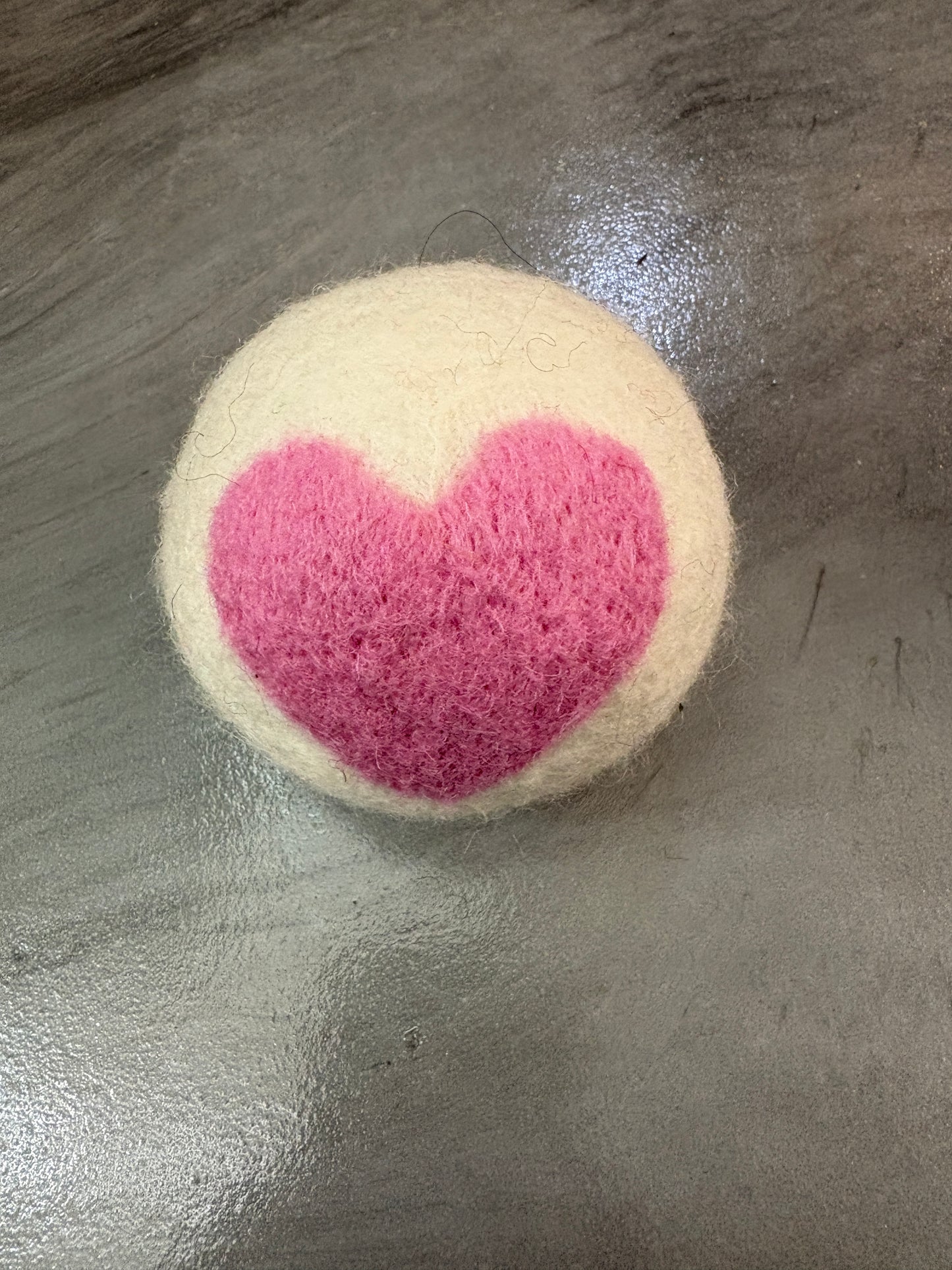 white wool dryer ball with pink heart design on a metallic surface