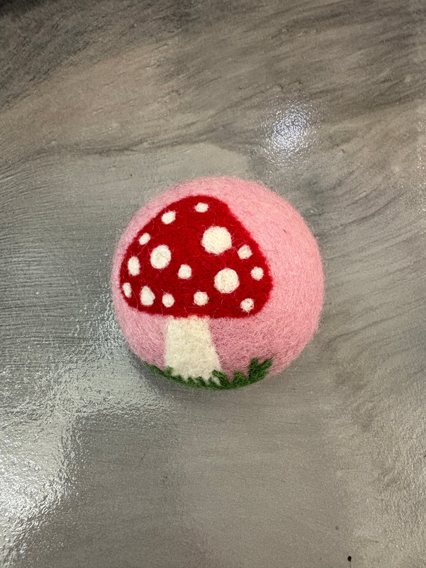 Pink wool dryer ball with a red mushroom-shaped object on a gray surface